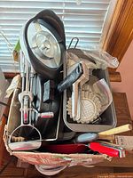 Overall view of box containing hand mixer, cookie press, loaf pan, tart molds, assorted utensils
