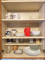 Wide view of cabinet shelves showing mugs, bowls, plates, pitcher and glasses