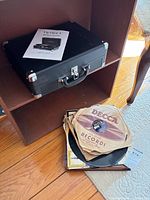 Suitcase turntable, manual on top, stack of vintage records in sleeves