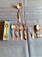 All eight pieces laid out on table: boxed commemorative spoon, child teaspoon, three forks, food pusher, curved baby spoon, Birks ladle