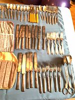 Overall view of cutlery arranged on cloth including knives, forks, spoons and fabric rolls