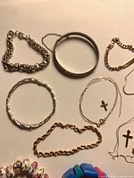 Overview showing silver link bracelet, plain bangle, rope bangle, gold ball bracelet, broken cross chains and fun bracelets