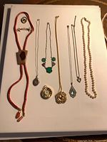 All items laid out: bolo tie, necklaces, pendant watches, brooches, pearls