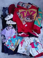 Pile of clothing showing red Taz hoodie, shorts, sneakers, additional garments beneath