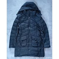 Full view of black Nike long puffer jacket, hood up, front zip, patch pockets visible