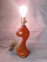 Full view lamp lit with bulb showing sculptural wood base and cord