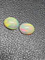 Pair of oval opals on textured black background showing body color and play-of-color