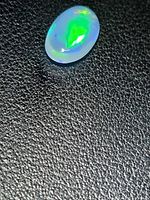Oval cabochon opal showing bright green flash on black background