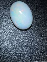 Full view of oval cabochon opal on black background