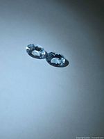 Two oval faceted pale blue aquamarine gemstones on neutral background