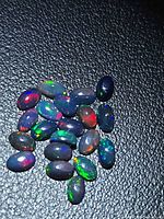 Group of oval black opal cabochons on textured black background