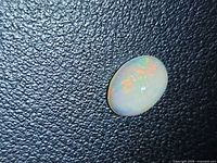 Oval Ethiopian opal showing multicolored fire on textured black background