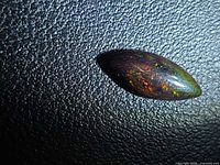 Marquise black opal on textured background showing play-of-color