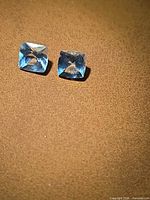 Two cushion-cut aquamarine stones on surface, showing color and cut