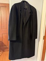 Full view of the black Christian Aujard overcoat hanging to show style and condition