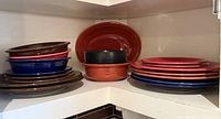 Stacks of Fiesta plates, bowls and red oval platter in cabinet