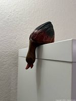 Front angled view of duck figurine hanging over white cabinet edge