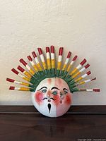 Front view of painted coconut shell mask with multicolor dowel headdress