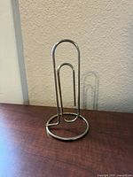 Full view of tall chrome paperclip stand on wooden surface