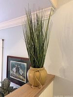 Full view of ceramic vase with faux grass on ledge