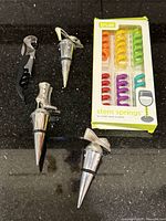 Wine accessories on black countertop: corkscrew, four chrome stoppers, sealed True Stem Springs pack
