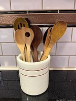 Ceramic crock with multiple wooden utensils displayed on countertop