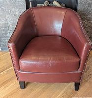 Front view of burgundy bonded leather barrel chair showing seat, nailhead trim and legs