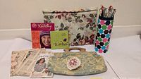 Group shot of all items including handbag, project pouch, needle holder, pincushion, books and patterns