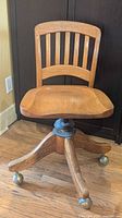 Front view of oak swivel office chair with slatted back and brass casters