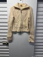 Full view of cream cable-knit zip sweater on hanger