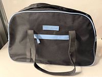 Front view showing black fabric, light blue piping, twin handles and logo patch