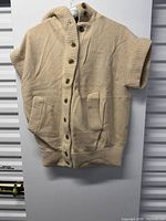 Front view of beige hooded vest showing sleeves, pockets, ribbed hem