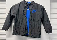 Front view of black Nike hooded jacket showing blue swoosh, pockets and blue fleece lining