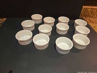 Twelve white ceramic ramekins arranged on dark surface