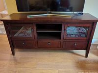 Front view of dark brown TV stand with TV on top, showing glass doors, drawers, open shelf