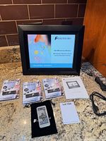 All items laid out: frame powered on, remote, three sealed USB drives, cable, adapter, manual