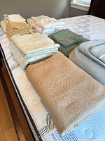 Stacks of folded King bedding pieces on bed: quilt, sheets, duvet cover, pillowcases