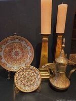 Group view of plates, candlesticks with candles and brass ewer