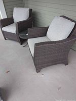 Two brown rattan patio armchairs with cushions and side table on porch