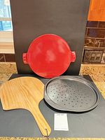 All three items: red Emile Henry pizza stone, Wilton perforated pan, wooden peel