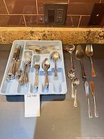 Overview of flatware set in tray with additional serving pieces on countertop