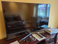 Front view of Samsung 55-inch TV on console with stand legs, DVD player, remotes, cables and paperwork visible