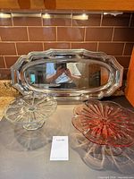 Front view of all three items: silver tray, pink stand, clear stand