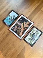 All three framed artworks laid out on wooden floor