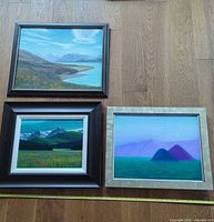 Three framed landscape paintings laid out on floor