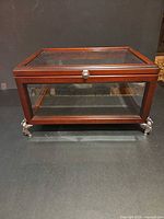 Front angled view of closed mahogany glass display case on decorative feet