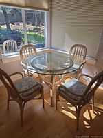 Dining set: glass-top table with four rattan chairs at window