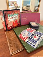 Overview showing trivia game box, Scrabble box, stack of card decks, cribbage board on green backgammon case