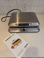 Closed waffle maker with manual beside it, showing overall item and accessory