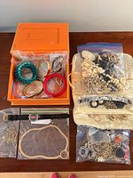Lot overview showing orange box with assorted bangles, bracelets, watch, jewelry cases and bagged items